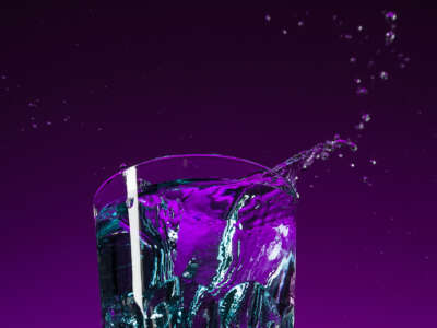 A glass of water splashes in front of purple-lit backdrop