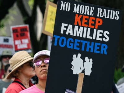A person holds a sign that reads "NO MORE RAIDS; KEEP FAMILIES TOGETHER" during an outdoor protest