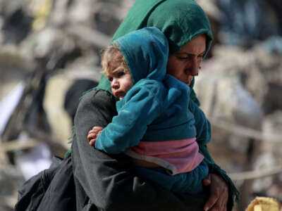A Palestinian woman carries a baby as families leave the eastern sector of the Gaza Strip on the border with Israel following Israeli airstrikes that targeted northern and other parts of Gaza in the early hours of March 18, 2025.