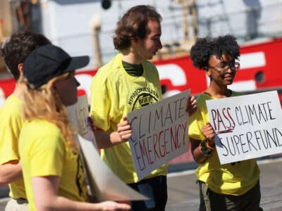 People hold signs during a press conference on the Climate Change Superfund Act at Pier 17 on May 26, 2023, in New York City. Representatives Daniel Goldman and Jerry Nadler were joined by state lawmakers as they spoke of the importance of passing the bill to make corporate polluters pay for the damages caused by climate change.