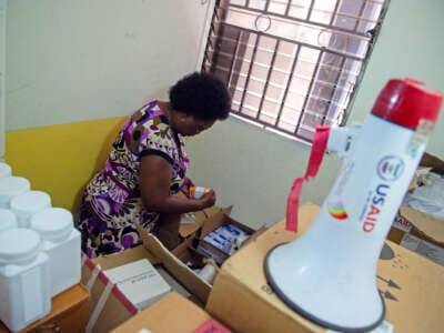 A nurse searches through boxes as a megaphone with a "USAID" logo on it is seen in the foreground